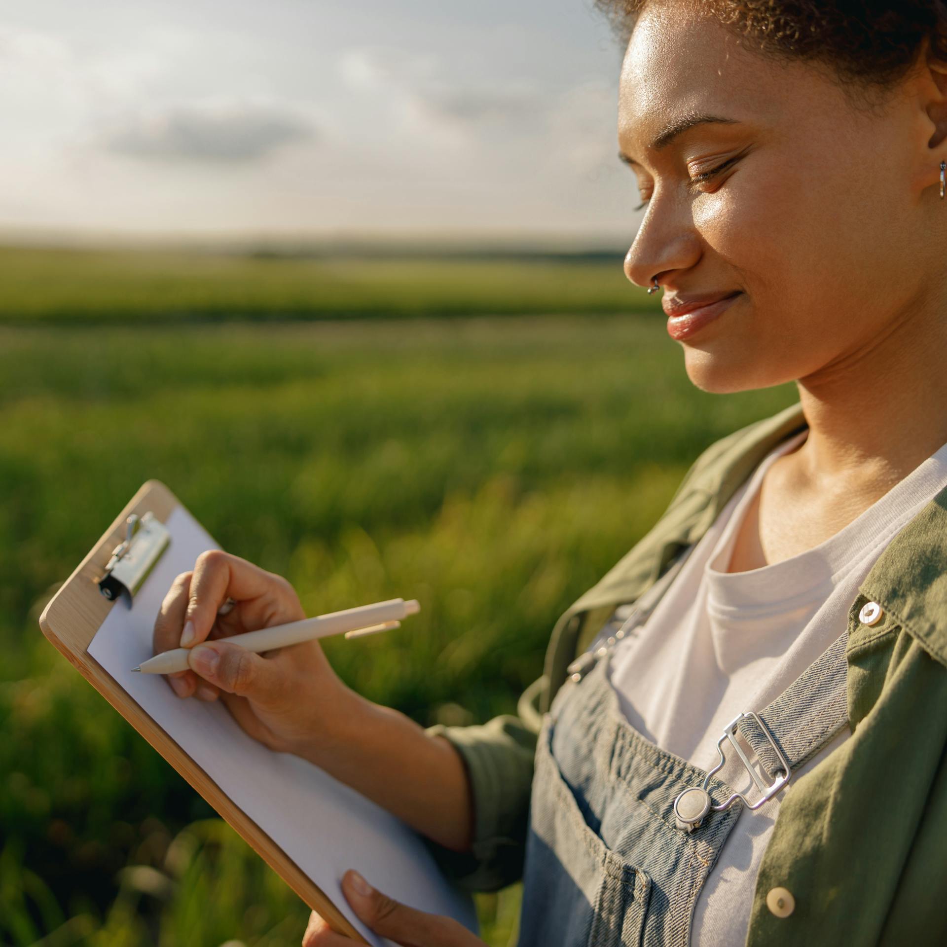 A woman in a sunny field writing notes on a clipboard