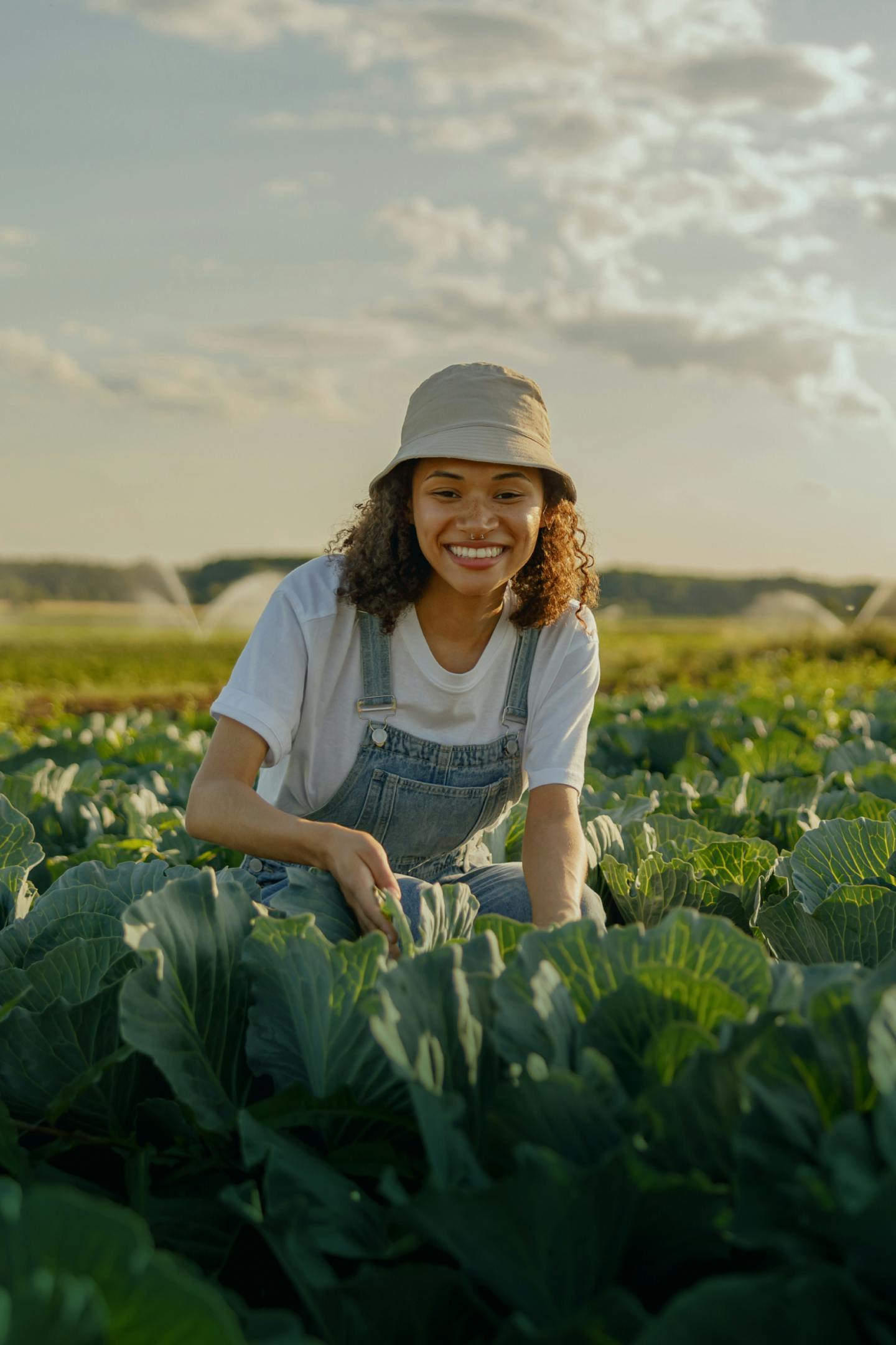 Image of woman in a cabbage farm, picking cabbages smiling in the sun