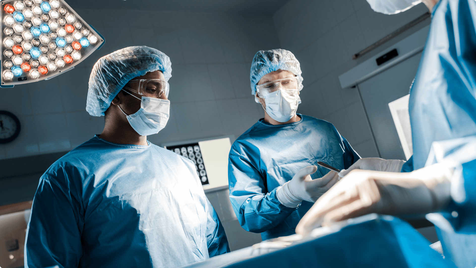 Three surgeons in full scrubs and surgical masks in an operating theatre carrying out an operation