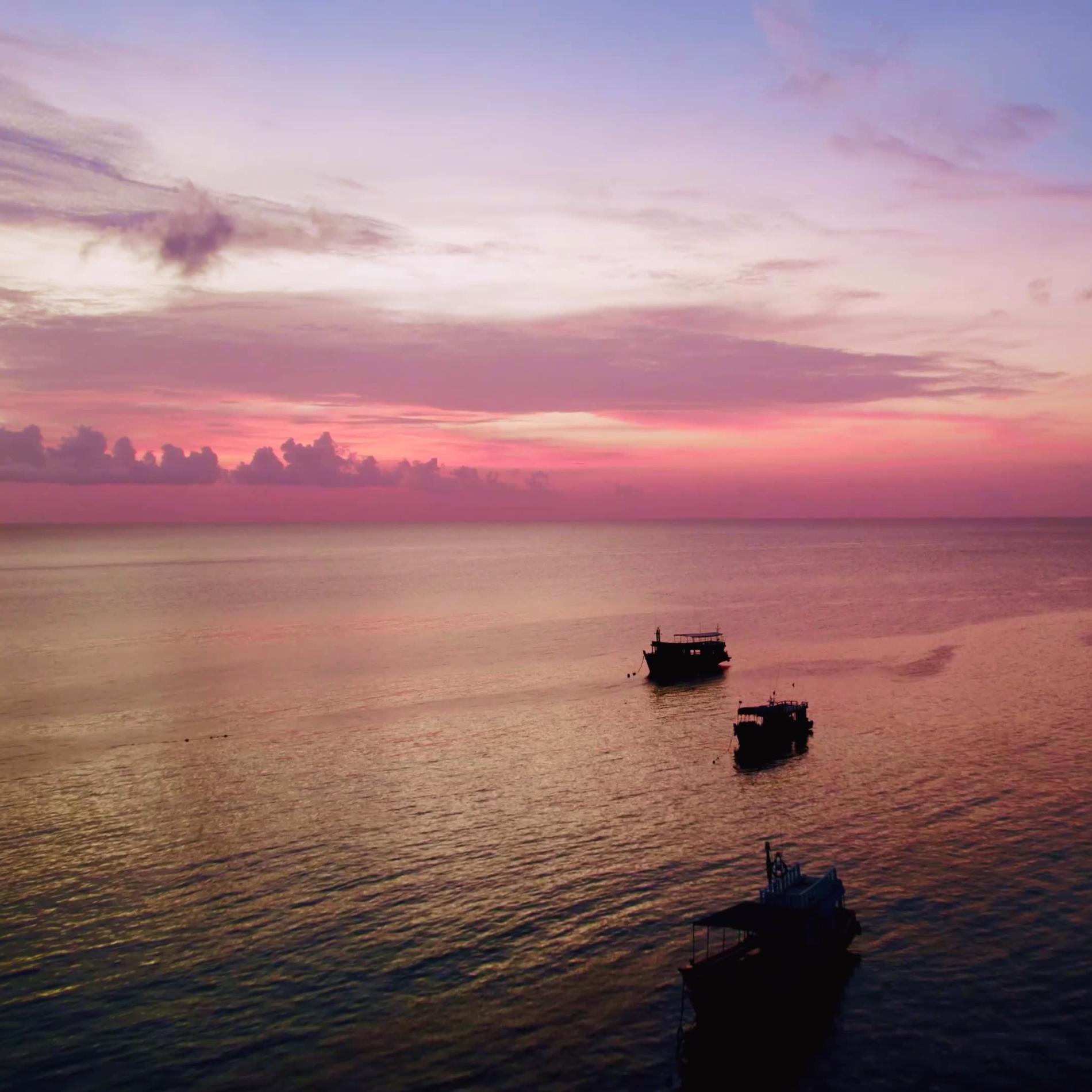 An image of a pink and purple sunset over water with boats.