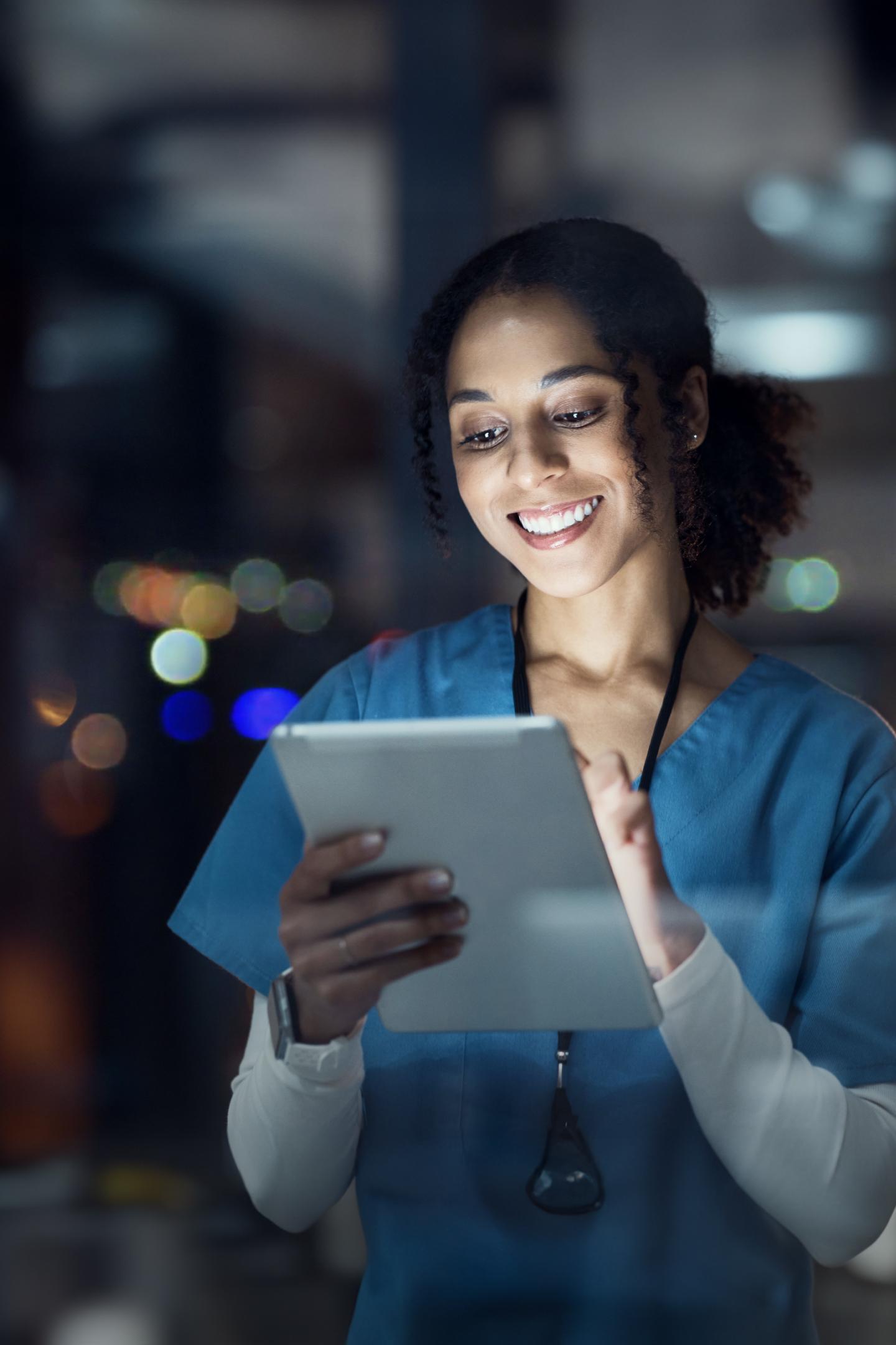 Image of a nurse at working at night using a tablet. the light is illuminating her face