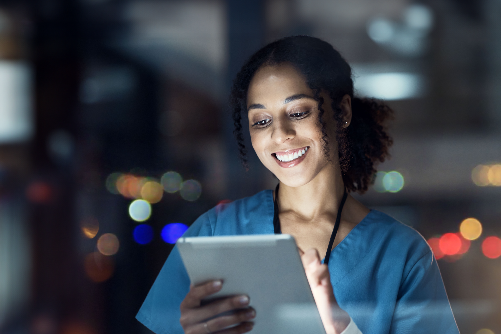 Medical professional in blue scrubs looks at a tablet screen smiling
