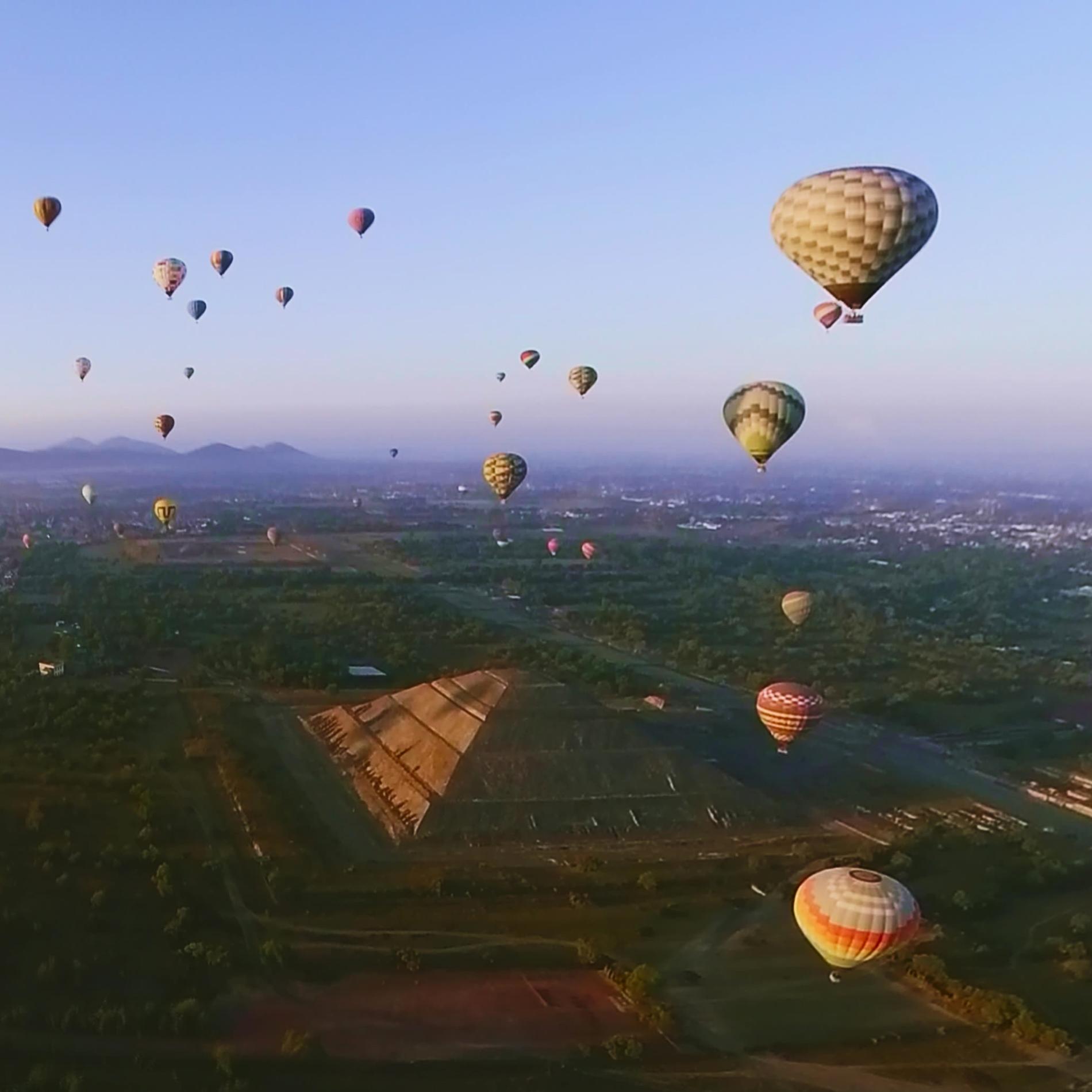 Hot air balloons fly over green land - around 30 of them