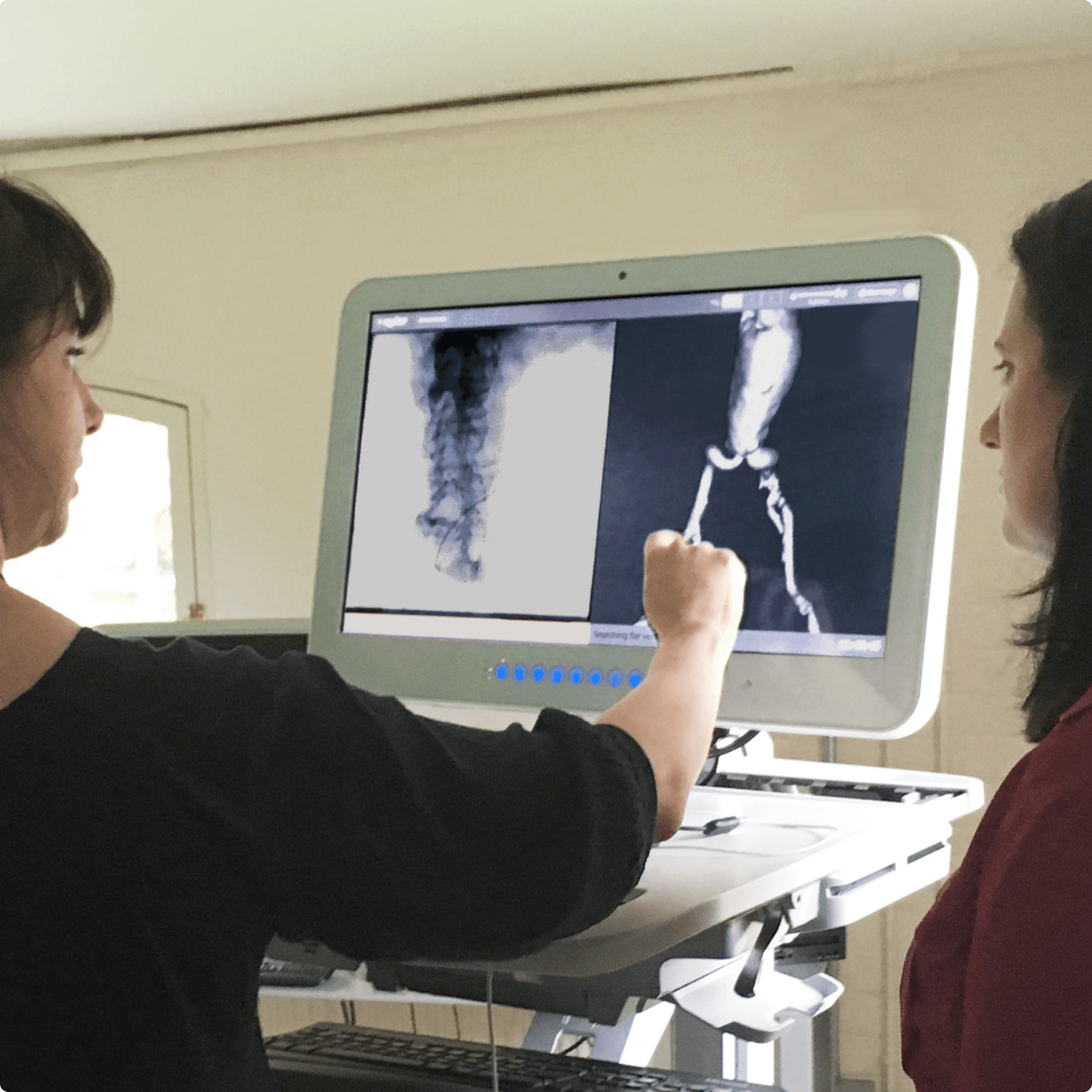 Two women are standing in front of a screen showing some images of a heart, one woman is interacting with the screen.