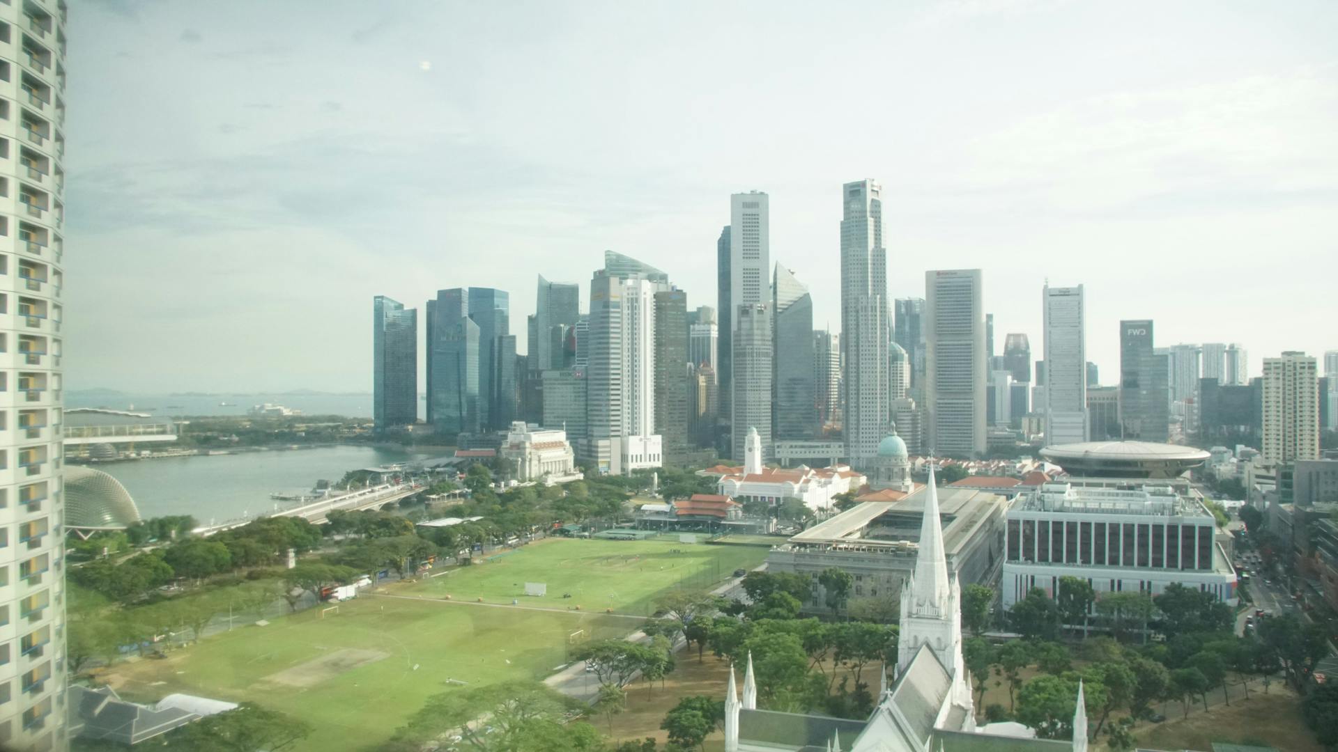 A photograph taken out of a window of the Singapore skyline with a park un the foreground