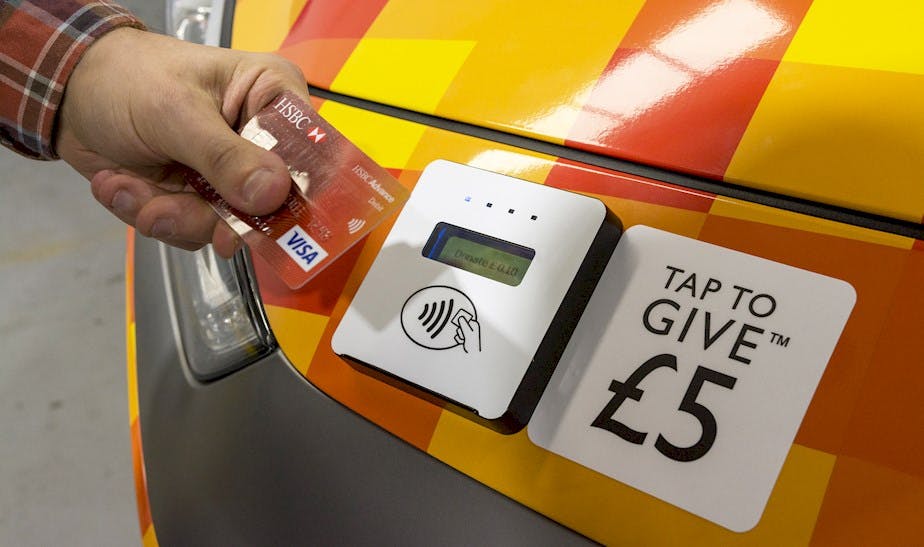 A person using a contactless donation point which is attached to a car. 