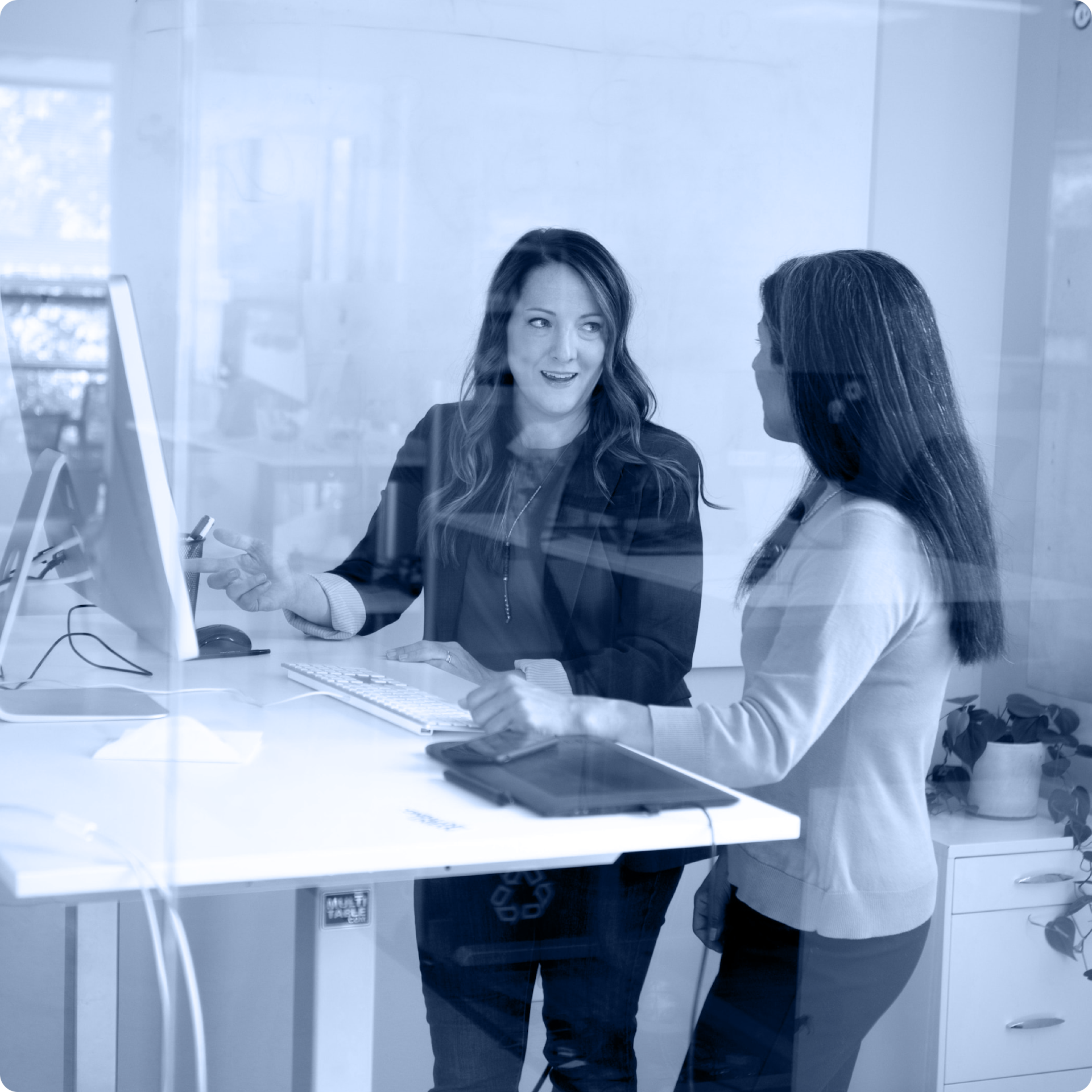 A photo of two people with long hair talking at a standing desk.