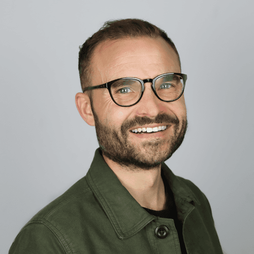 George smiles at the camera. He is wearing glasses and a green shirt. 