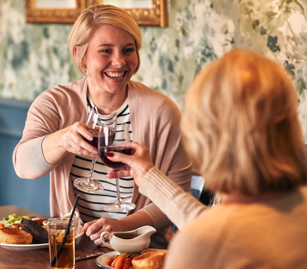Two women drinking in a bar over food, one has their back to the camera. Two women drinking in a bar over food, one has their back to the camera.