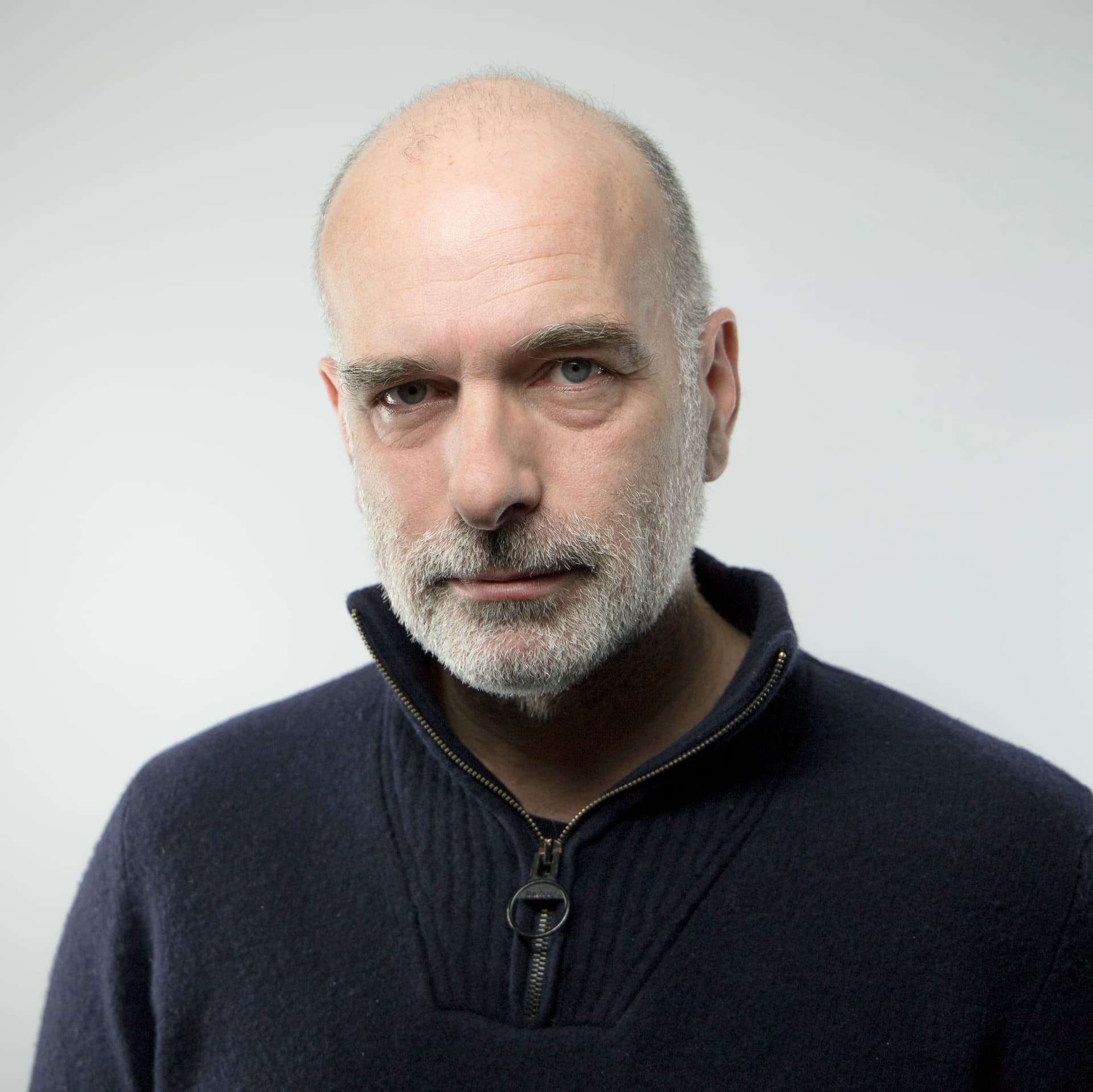 Tim wears a navy zip up sweatshirt, he is looking at the camera. Tim wears a navy zip up sweatshirt, he is looking at the camera.