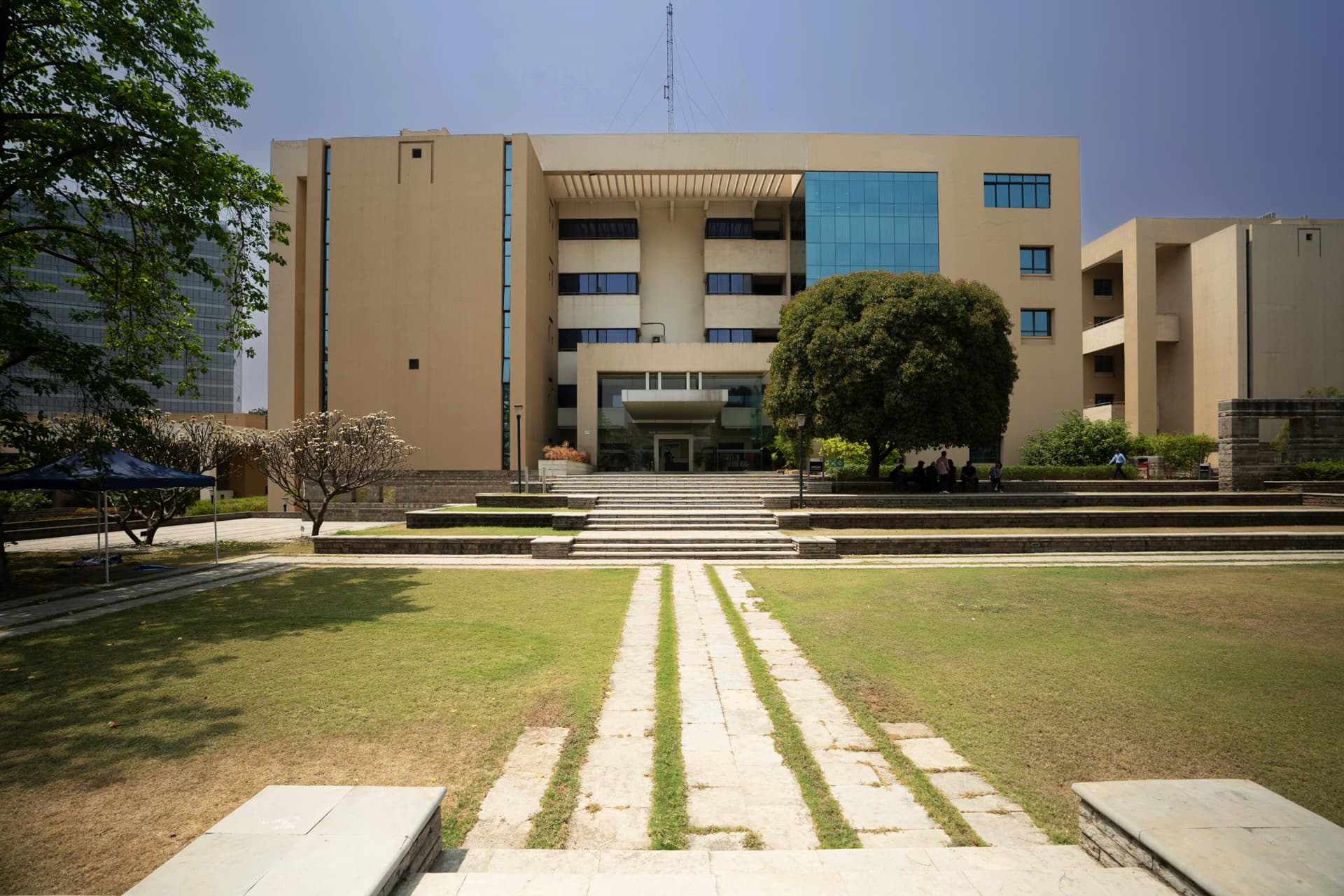 A large light yellow building, with reflective windows sits behind a green lawn and a path. It's a sunny day. This is the Pune, India office, Zensar Knowledge Park. A large light yellow building, with reflective windows sits behind a green lawn and a path. It's a sunny day. This is the Pune, India office, Zensar Knowledge Park.