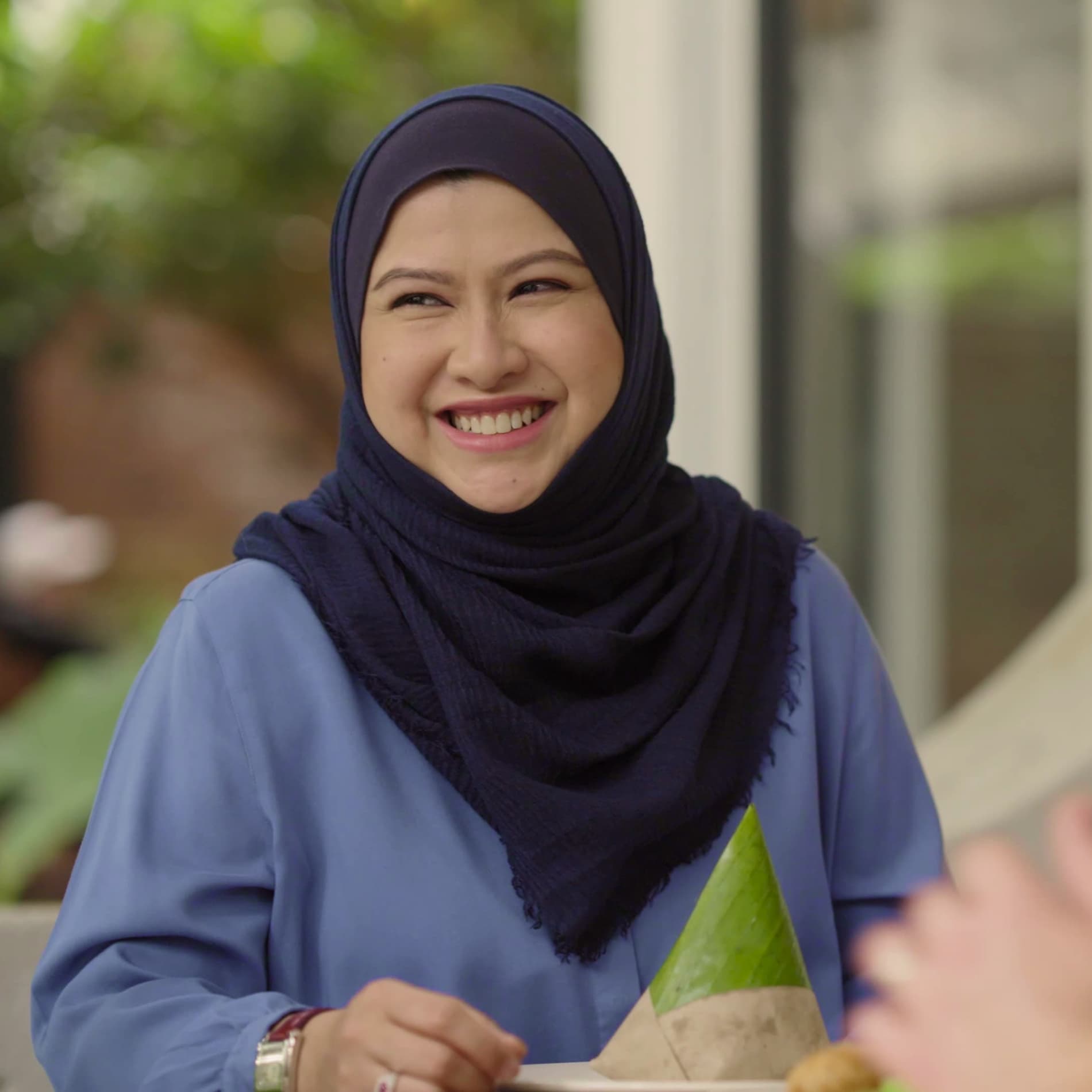 A woman in blue wearing a navy head covering smiles. A woman in blue wearing a navy head covering smiles.