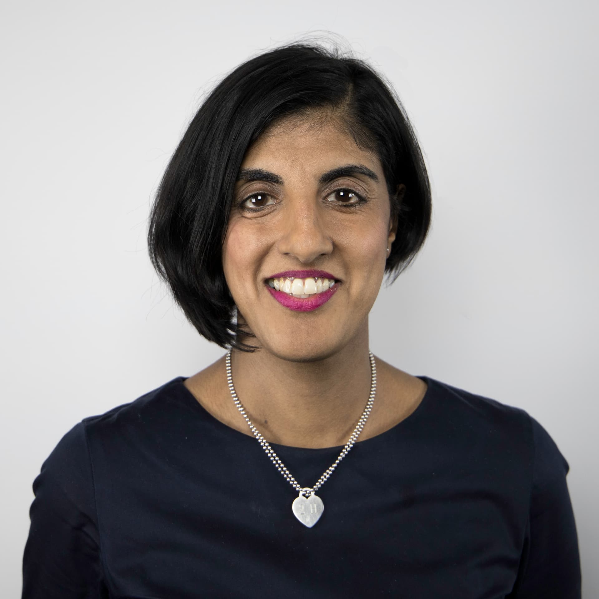 Harpal smiles at the camera. She is wearing a black top and a silver necklace. Harpal smiles at the camera. She is wearing a black top and a silver necklace.
