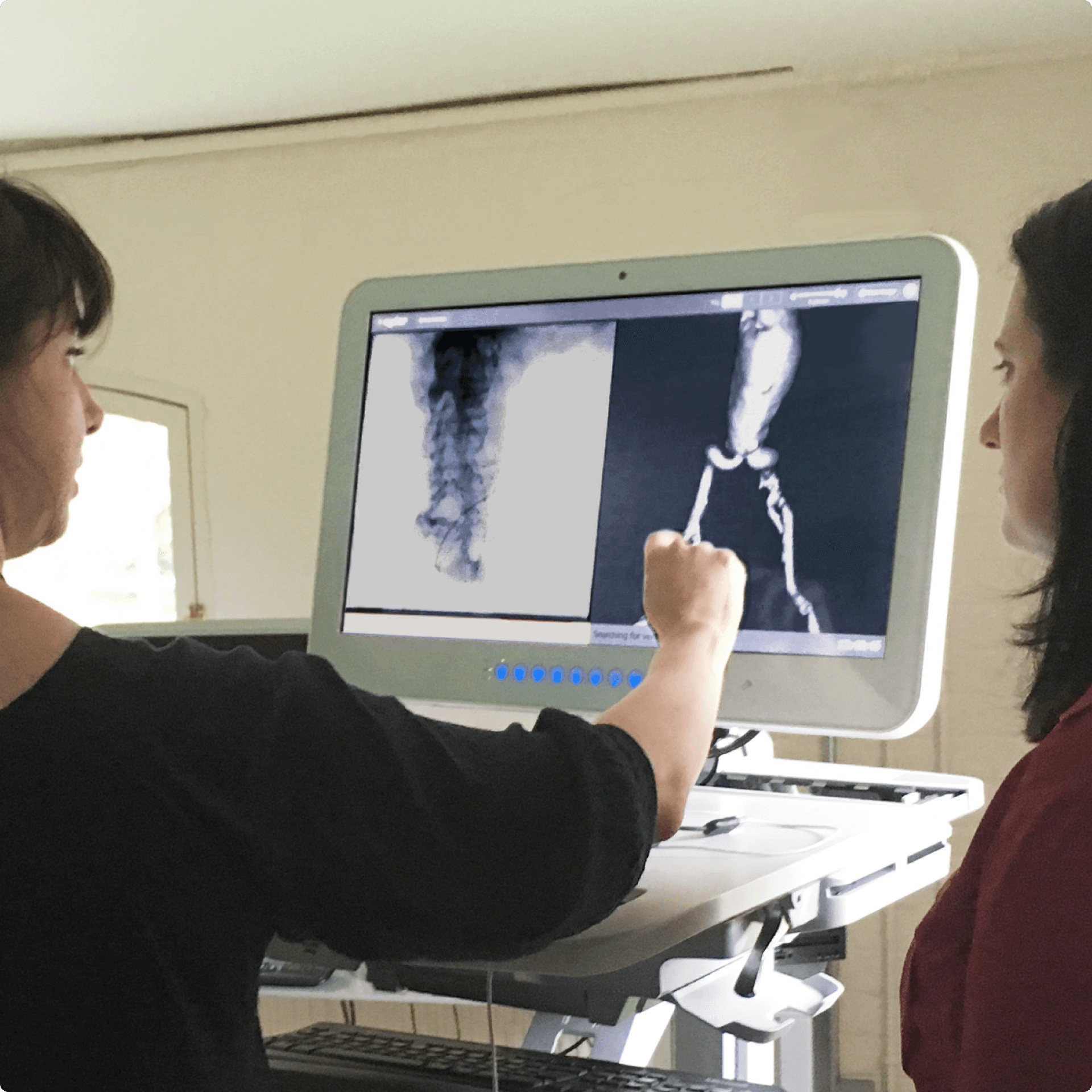 Two women are standing in front of a screen showing some images of a heart, one woman is interacting with the screen. Two women are standing in front of a screen showing some images of a heart, one woman is interacting with the screen.