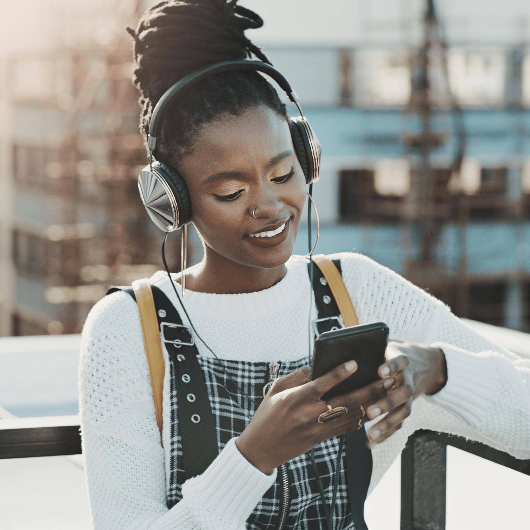 A woman is outside wearing headphones, she's looking at her phone.