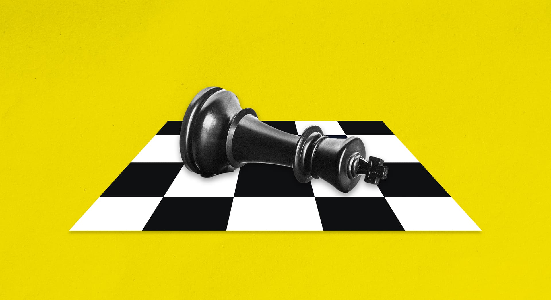 A chess piece is on its side on a chess board, on a yellow background. 