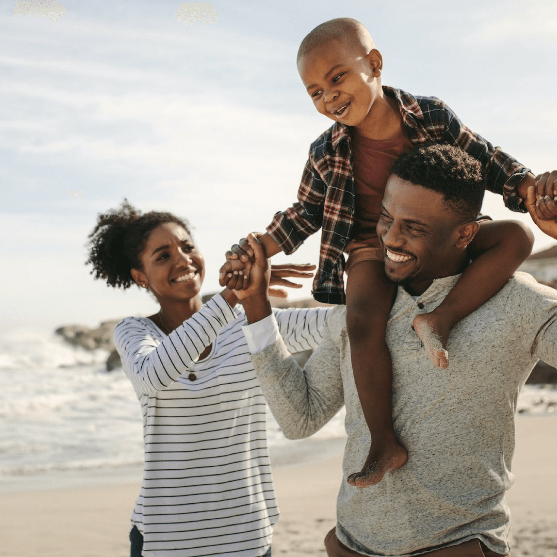 A happy family at the beach, with a child on the father's shoulders.